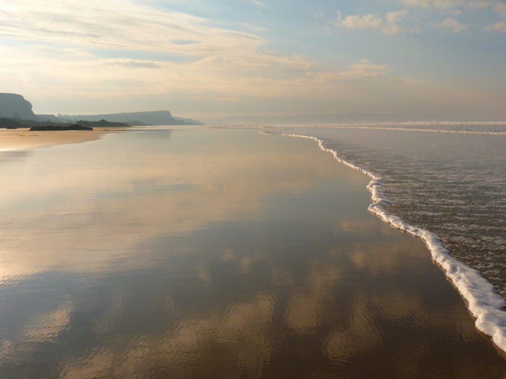 Photo by Robin Rowling of waves lapping a large sandy beach between Northcott Mouth and Crooklets Beach