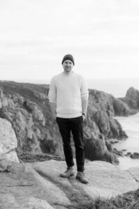 Black and white photo of Gareth Rees standing on a cliff top. Photo by Rebecca Rees Photography